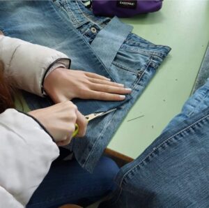 in primo piano mani di studenti che tagliano dei jeans blue