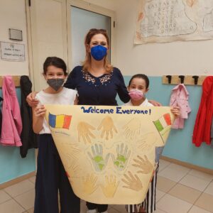 Due alunni della scuola primaria, con la maestra all'interno di un'aula mostrano un cartellone di benvenuto