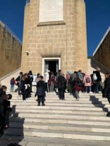 studenti su una scalinata in pietra di colore chiaro si apprestano ad entrare in una porta centrale che condurrà alla cripta del monumento