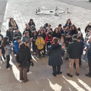 Studenti fotografati dall'alto disposti a semicerchio davanti alla guida turistica che, posta di spalle, staparlando loro