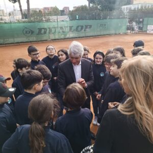 Gruppo di persone in primo piano: il Ministro dello sport al centro, stringe la mano a studenti con felpa blu