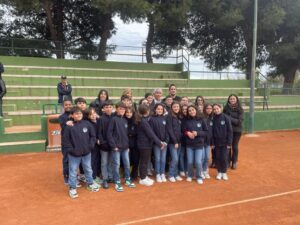 Scolresca con divisa scolastica in blu, preside, docenti e Ministro dello sport in posa nel campo di tennis