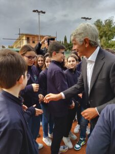 Gruppo di persone in primo piano: il Ministro dello sport al centro, stringe la mano a studenti con felpa blu