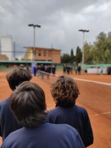 In primo piano studenti di spalle, guardano il campo di tennis, sullo sfondo un gruppo di persone